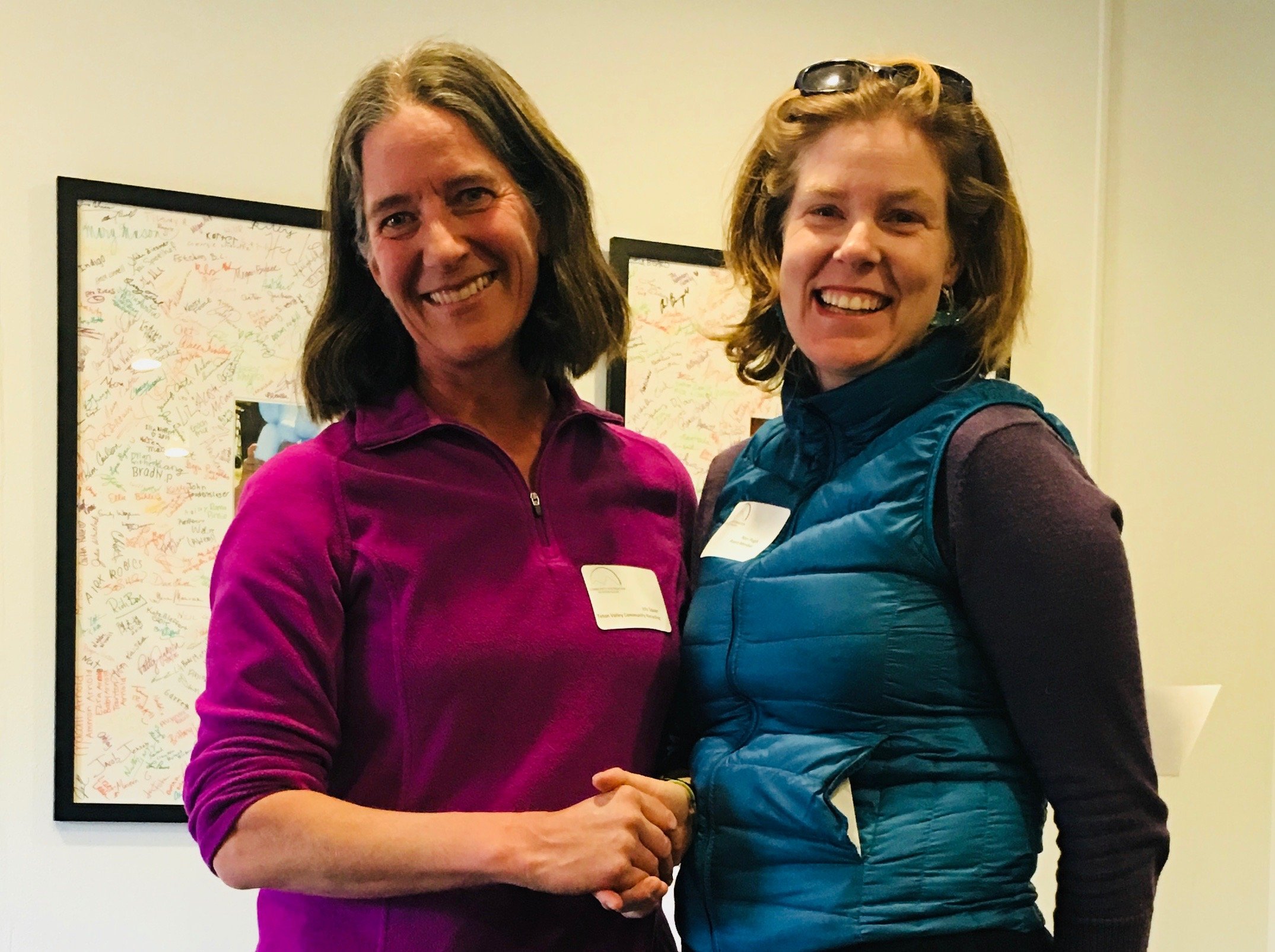 Teton Valley Non-Profits, In a scene brimming with warmth and collaboration, two women are captured smiling and shaking hands indoors, amidst an atmosphere enriched by framed artwork adorning the walls. One woman, dressed in a purple top, radiates enthusiasm as she extends her hand to her companion. The other woman, sporting a blue vest complemented by sunglasses perched atop her head, exudes vibrant energy.

This moment symbolizes the profound impact of the Community Foundation of Teton Valley's support for non-profits and local businesses. Through charitable giving, this foundation not only fosters dynamic partnerships but also enhances the cultural tapestry and economic vitality of the community. By investing in these meaningful relationships, they lay down strong roots for collective growth and prosperity. The Tin Cup Challenge & Run is the CFTV annual giving event day.