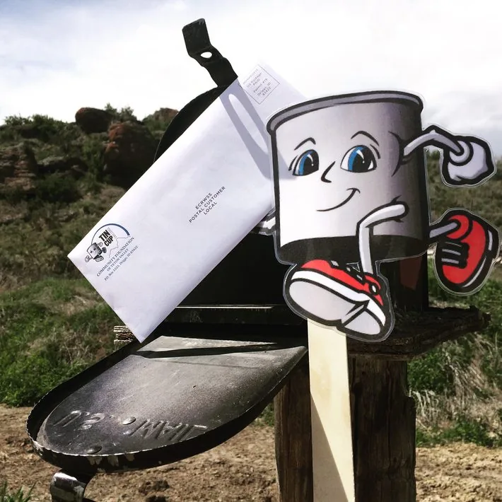 A Tin Cup Challenge mascot beside a mailbox holding the 19th Annual Tin Cup Challenge mailer
